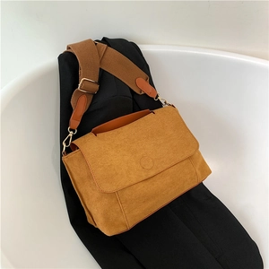 Sac bandoulière en daim marron avec large sangle porté sur une veste de blazer noire