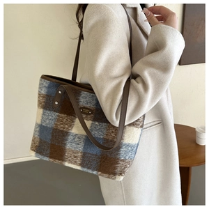 Detail of checkered tote bag featuring brown leather straps and vintage metallic logo plaque