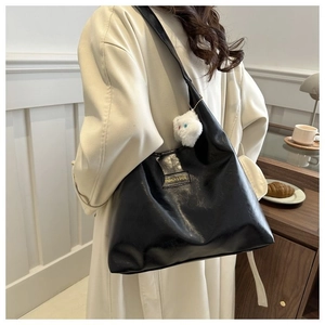 Close-up of black leather tote bag featuring a plush cat charm and fashion logo detail