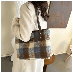 Detailed macro shot of vintage plaid wool tote bag with brown leather strap and metal logo