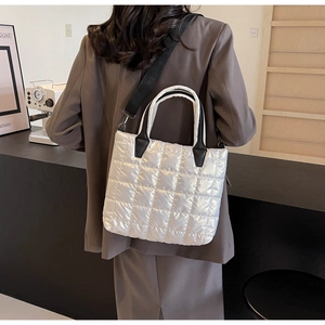 Stylish white quilted puffer tote bag with black strap worn by a woman in a suit