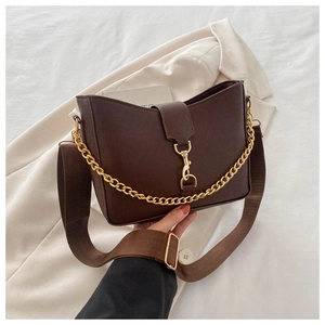 Close-up of brown leather bucket bag featuring a wide fabric strap and gold chain detail