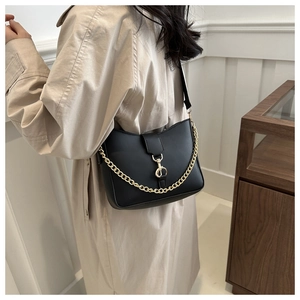 Detail of black matte leather shoulder bag featuring a chunky gold chain and metal clasp