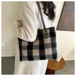 Detail of plaid tote bag with brown leather strap and woven tweed texture on side view
