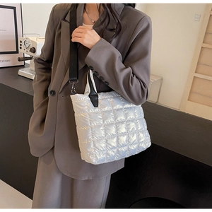 Silver quilted tote bag with metallic finish and wide black straps worn with a brown suit