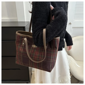 Macro detail of plaid tote bag featuring a gold metal logo and premium leather handles