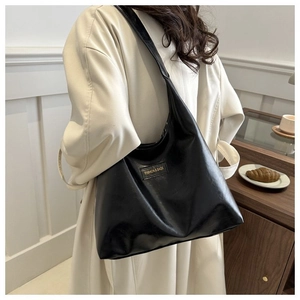 Detail of a large black faux leather tote bag showing the fashion label and wide shoulder strap