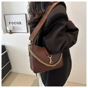 Detail of a dark brown leather bucket bag with a gold chain and woven wide strap
