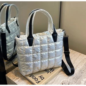 Detailed macro view of white quilted puffer bag featuring black handles and nylon strap