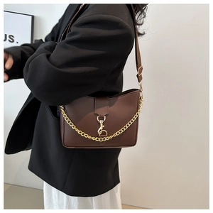 Detail of brown matte bucket bag with golden chain and clasp on a model shoulder