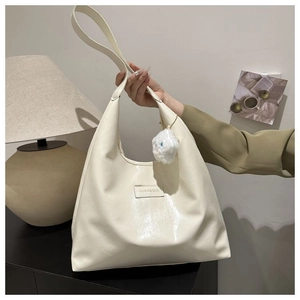 Detail of cream white tote bag featuring a silver fashion plaque and soft plush pendant