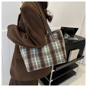 Detail of checkered woolen tote bag with brown leather straps and silver rivet reinforcement