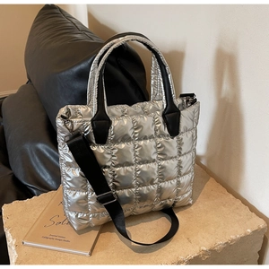 Detail of silver metallic quilted tote bag with black handles on a stone pedestal