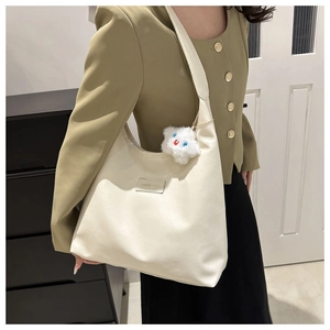 Detail view of a large cream hobo bag with fashion label and plush bear charm on model