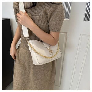 Detail view of cream bucket bag showing metal chain and wide fabric strap on model