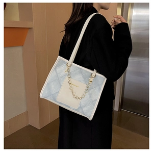 Détail du sac cabas en jean matelassé bleu clair avec poche blanche et chaîne dorée