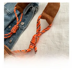 Detail of brown corduroy bag featuring a bright orange braided rope strap and metal tips