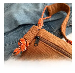 Detail of smooth metal zipper and cord strap on a brown corduroy crossbody bag
