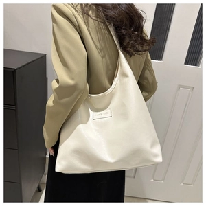 Detailed side view of a large cream-colored faux leather tote bag worn with a blazer