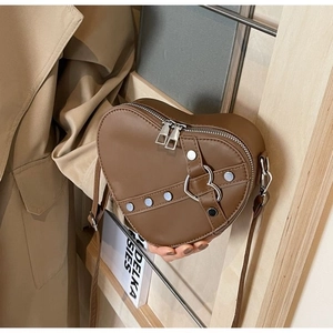 Detailed macro view of a brown heart-shaped crossbody bag with metal rivets and strap