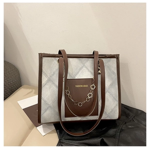Détail du sac cabas en toile matelassée bleue avec bordure en cuir marron et chaîne