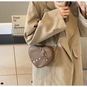 Detailed side view of a heart-shaped brown leather crossbody bag with silver rivet accents