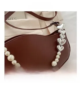 Detail of coffee brown bag featuring wavy edge design and pearl heart chain strap