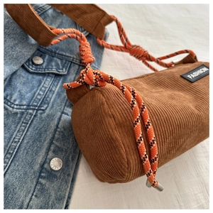 Detail of a brown corduroy cylindrical crossbody bag with orange woven rope strap and label