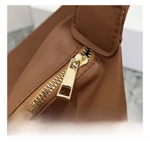 Detail of smooth light gold metal zipper on brown pebble leather shoulder bag