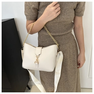Detail of a beige bucket bag with vintage gold clasp and wide fabric strap on model