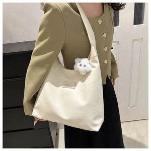 Close-up of cream large hobo shoulder bag with plush pendant on olive blazer