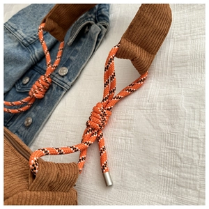 Detail of brown corduroy crossbody bag with woven tri-color rope strap and metal caps
