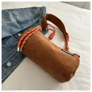 Detailed macro view of a brown corduroy cylindrical crossbody bag with woven rope handle
