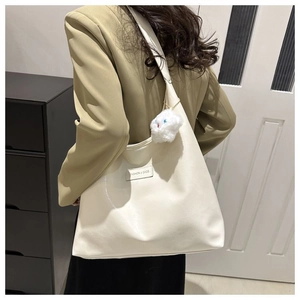 Close-up of off-white tote bag with plush charm and fashion label on shoulder