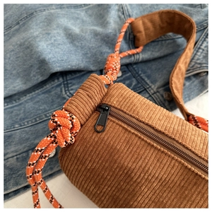 Detailed close-up of brown corduroy barrel bag texture with woven rope strap