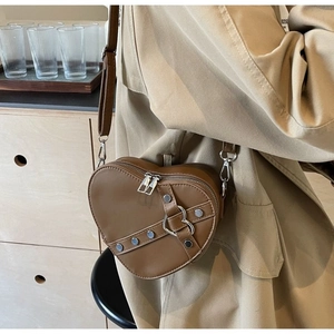 Close-up of a brown heart-shaped leather crossbody bag with silver buckle and stud details