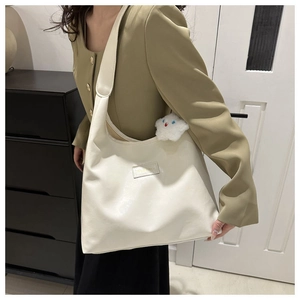 Detail of a large beige tote bag with a star plush charm and a stylish square logo patch