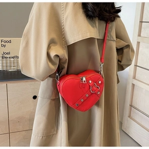 Macro shot of red heart-shaped leather crossbody bag with silver rivet details and strap