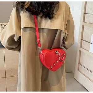 Close-up of heart-shaped red crossbody bag with silver studs on khaki trench coat