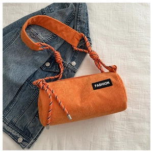 Detail of orange corduroy barrel bag with woven shoulder strap on blue denim
