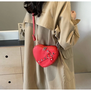 Detail view of red heart-shaped leather crossbody bag with silver rivets and metal buckle