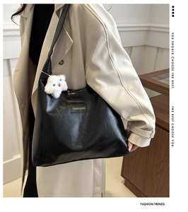 Detail of black soft PU leather tote bag with gold metal logo and plush cat pendant