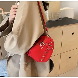 Detail of red heart-shaped crossbody bag with silver studs on khaki trench coat