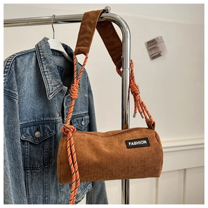 Detail of brown corduroy cylinder bag with orange woven rope strap and fashion label