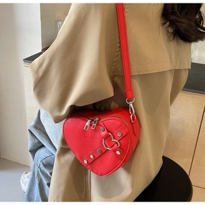 Detail view of red heart-shaped crossbody bag with silver studs and metal buckle on model