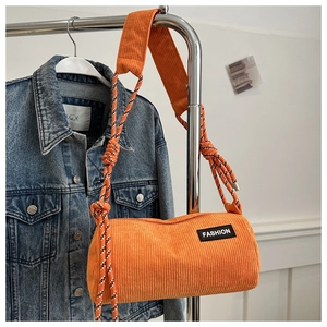 Close-up of orange corduroy cylinder bag with fashion label and braided rope strap