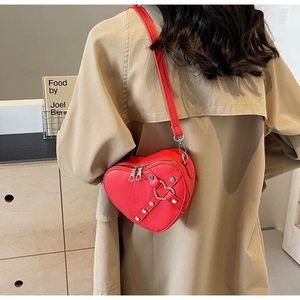 Detail of red heart-shaped crossbody bag with silver rivet straps and leather texture