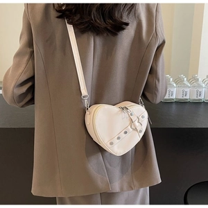 Model wearing a cream heart-shaped crossbody bag with stud detail and thin shoulder strap