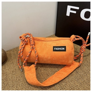 Detail of orange corduroy cylindrical crossbody bag featuring a black fashion label