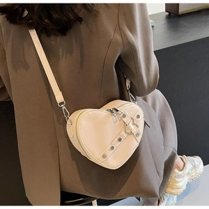Detail of a heart-shaped beige PU leather crossbody bag with studs on a person